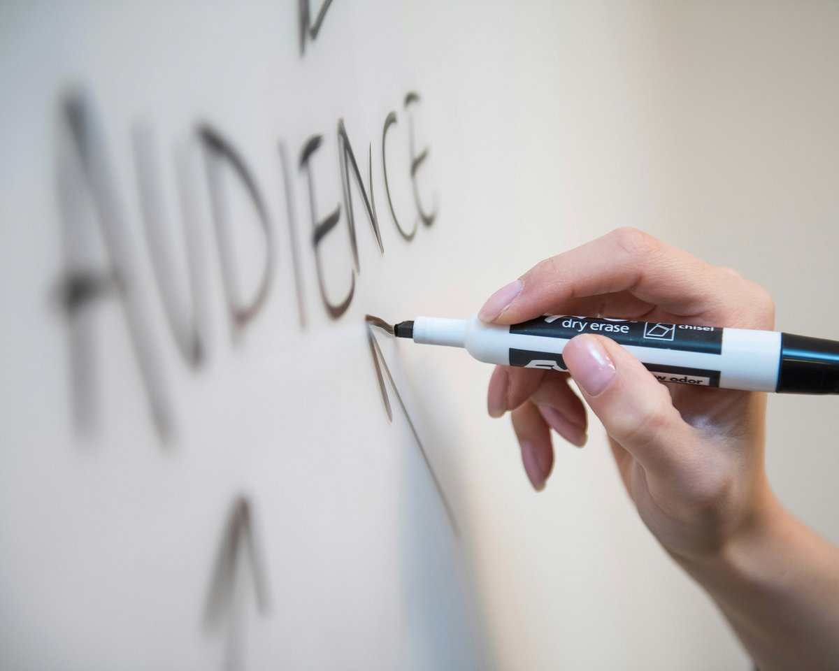 Hand schreibt das Wort „Audience“ an ein Whiteboard